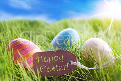 Three Colorful Easter Eggs On Sunny Green Grass With Label Happy Easter