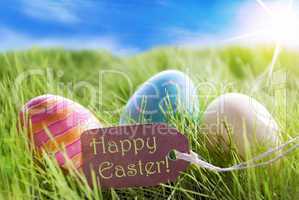 Three Colorful Easter Eggs On Sunny Green Grass With Label Happy Easter