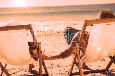 Cute couple holding hands while lying on their deck chairs