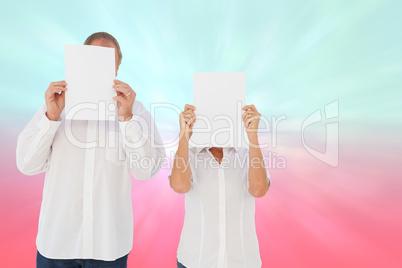 Composite image of couple holding paper over their faces