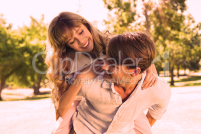 Man giving his pretty girlfriend a piggy back in the park smilin