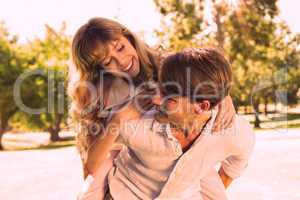 Man giving his pretty girlfriend a piggy back in the park smilin