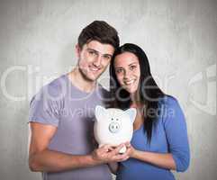 Composite image of young couple holding a piggy bank