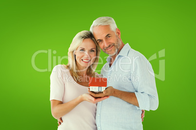 Composite image of happy couple holding miniature model house