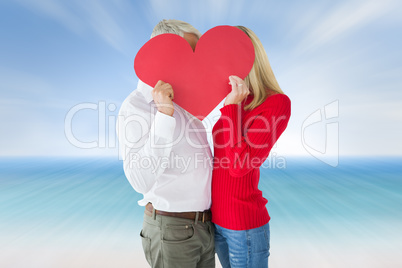 Composite image of couple embracing and holding heart over faces