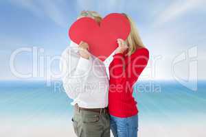 Composite image of couple embracing and holding heart over faces