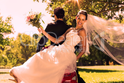 Newlywed couple sitting on scooter in park