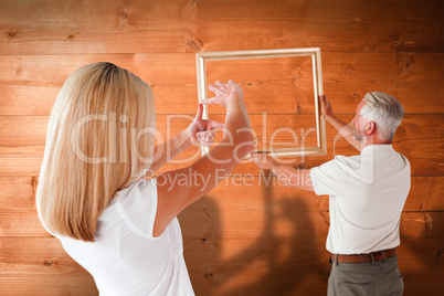 Composite image of couple hanging a frame together