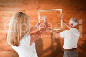 Composite image of couple hanging a frame together