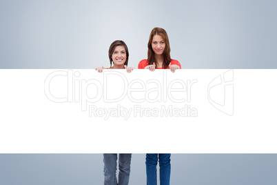 Composite image of smiling young women proudly holding a blank p