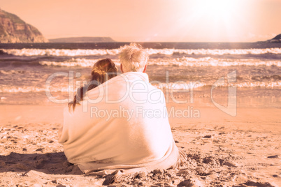 Couple sitting on the beach under blanket looking out to sea