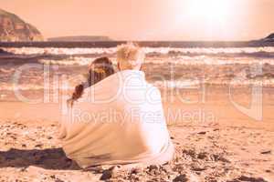 Couple sitting on the beach under blanket looking out to sea