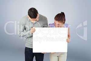 Composite image of young couple holding banner together and look