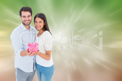 Composite image of happy couple showing their piggy bank