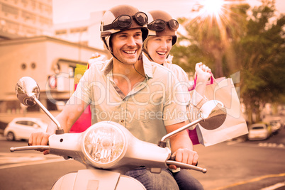 Hip young couple riding scooter with shopping bags