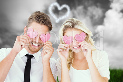 Composite image of attractive young couple holding pink hearts o