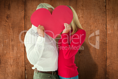 Composite image of couple embracing and holding heart over faces