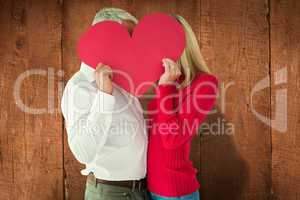 Composite image of couple embracing and holding heart over faces