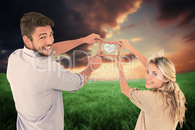 Composite image of attractive young couple hanging a frame