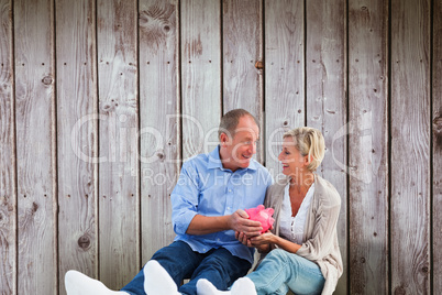 Composite image of happy mature couple holding piggy bank