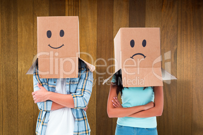 Composite image of young couple wearing sad face boxes over head