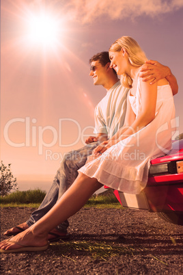 Cheerful couple sitting on their cabriolet car hood