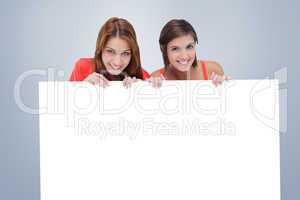 Composite image of teenage girls smiling while holding a blank p