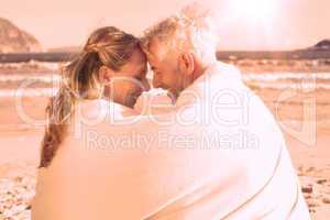 Couple sitting on the beach under blanket smiling at each other