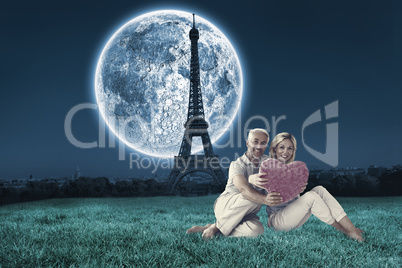 Composite image of happy couple sitting and holding heart pillow