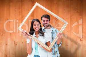 Composite image of happy young couple holding picture frame