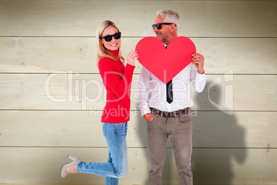 Composite image of cool couple holding a red heart together