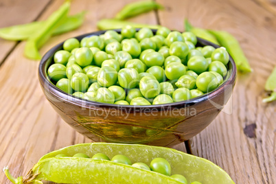 Green peas in brown bowl and pod on board