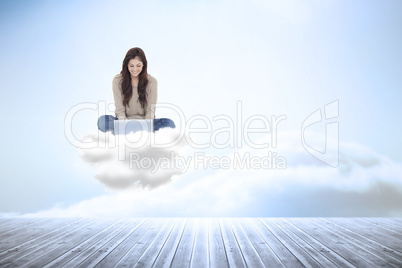 Composite image of brunette sitting on cloud using laptop