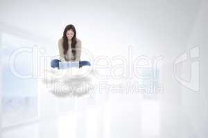 Composite image of brunette sitting on cloud using laptop