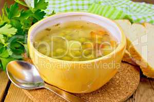 Soup of green peas in yellow bowl with bread on board