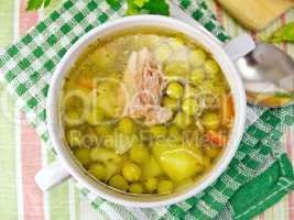 Soup of green peas with meat on tablecloth