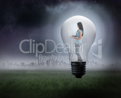 Composite image of woman holding laptop in light bulb