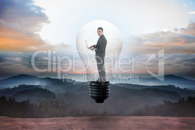 Composite image of businessman holding laptop in light bulb