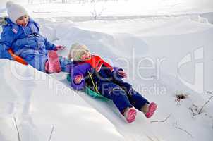 Two girls rolling down a hill in snow