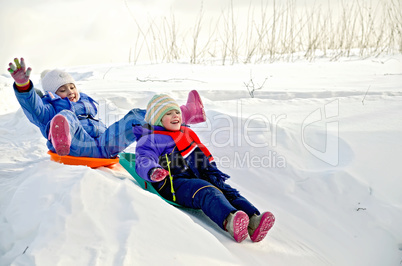 Two little girls on sled through the snow to slide