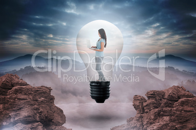 Composite image of woman holding laptop in light bulb