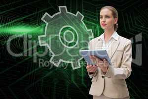 Composite image of cog and wheel and businesswoman using tablet