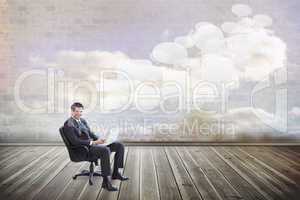 Composite image of young businessman sitting working with a lapt