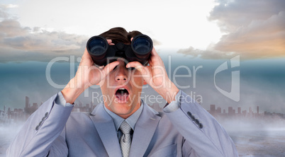 Composite image of suprised businessman looking through binocula