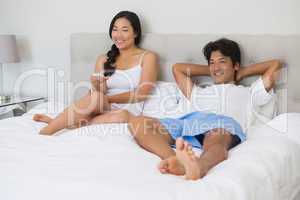 Happy couple lying on bed together watching tv