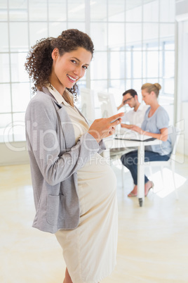 Pregnant businesswoman sending text with team behind her