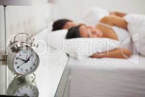 Couple lying in bed with focus on alarm clock