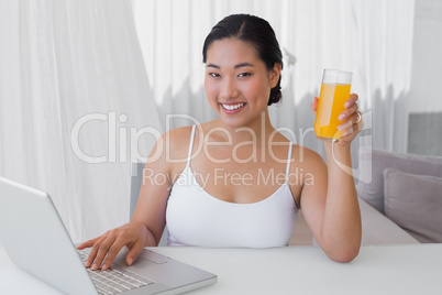 Happy woman using laptop and having orange juice