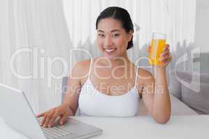 Happy woman using laptop and having orange juice