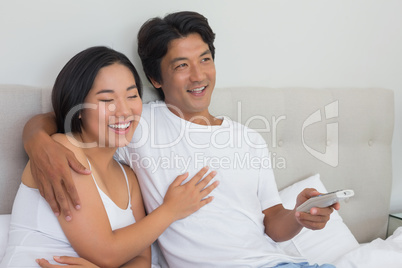 Smiling asian couple lying on bed watching tv